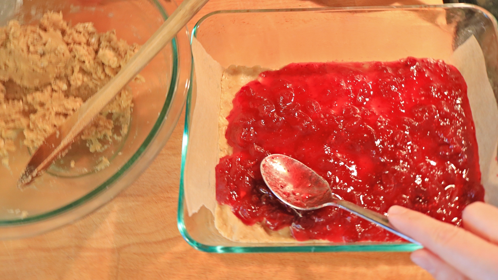 Spoon spreading cranberry sauce onto cookie bars.