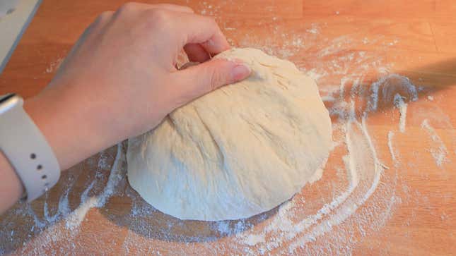 A hand grabbing a ball of dough on a countertop.