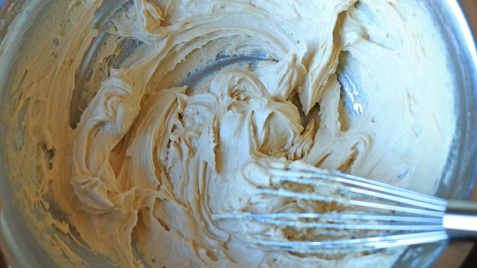 A whisk in a bowl with frosting.