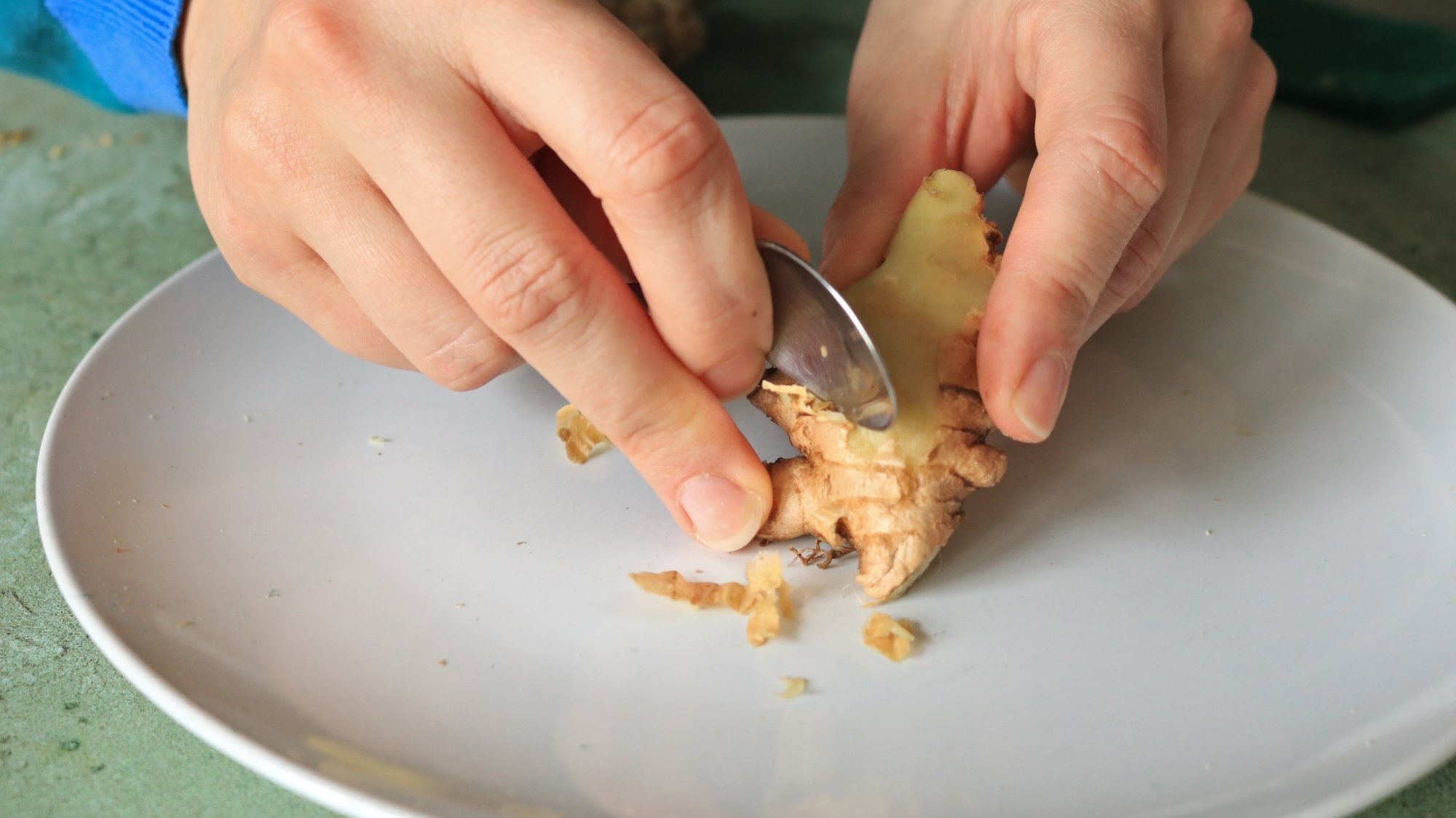 Hands peeling ginger with a spoon.