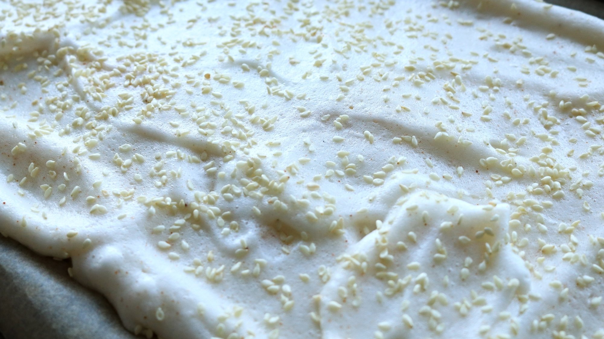 Meringue sprinkled with sesame seeds spread on a sheet tray.