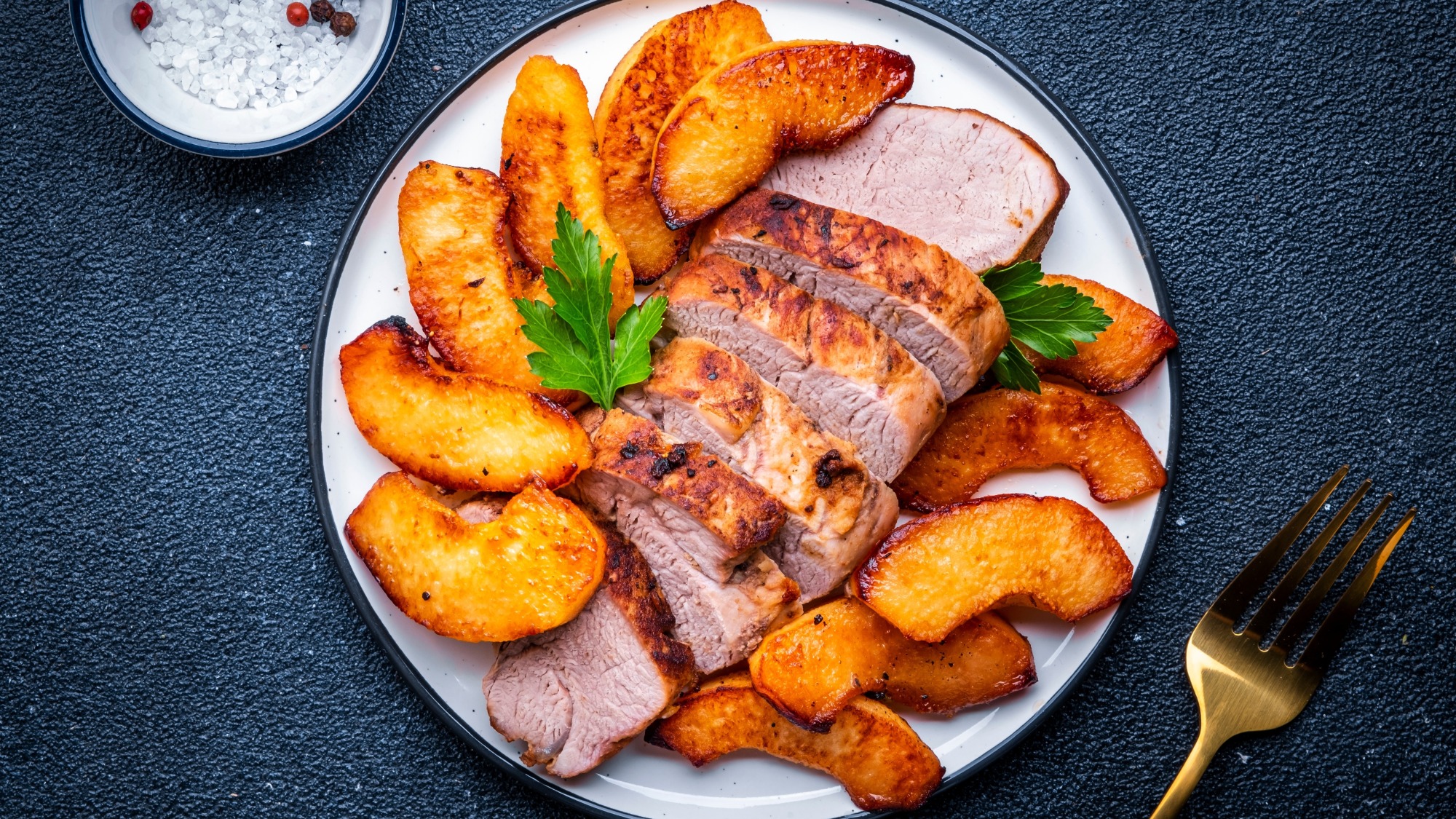 Roasted pork sliced on a plate with roasted apple slices.