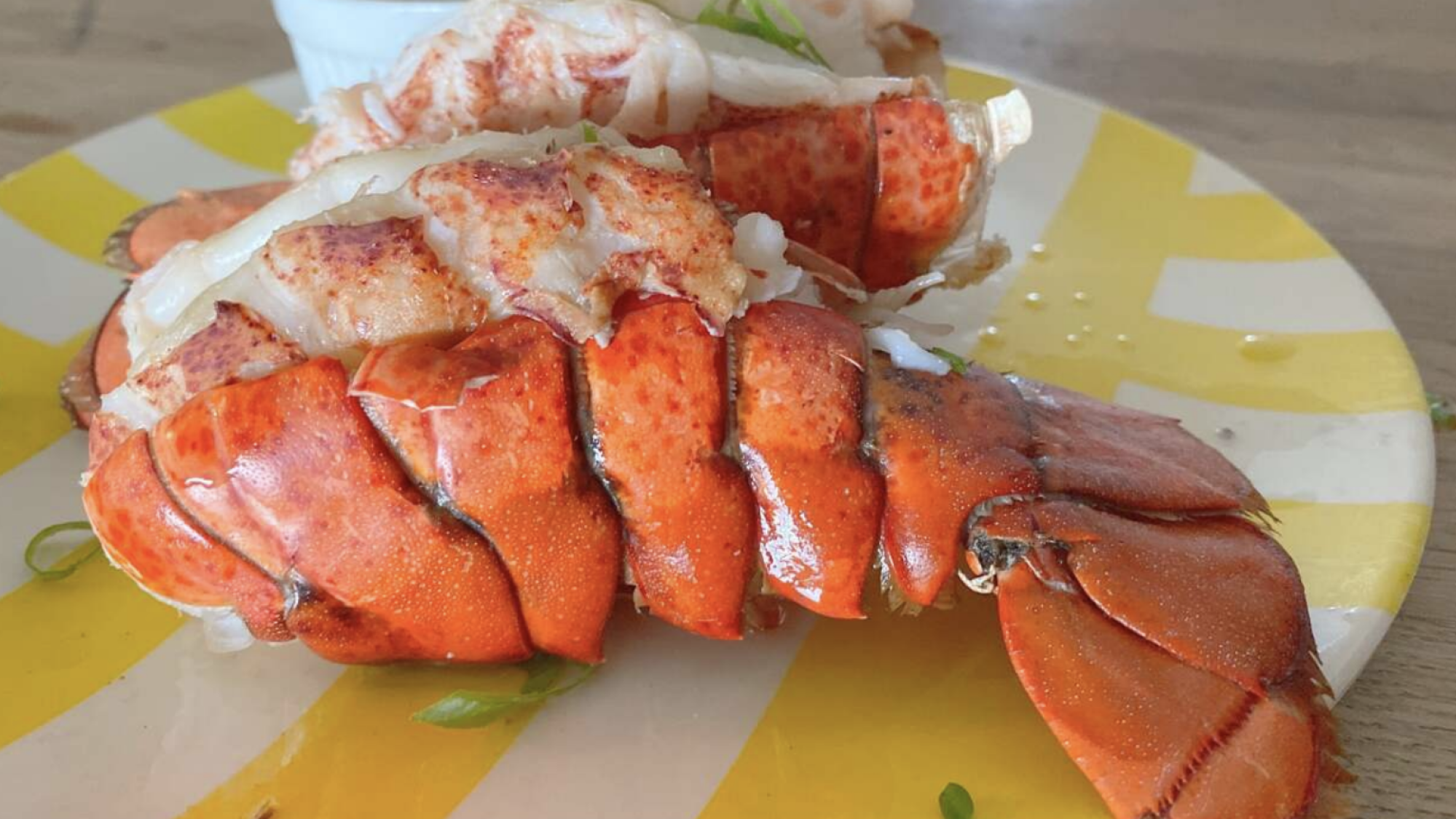 Two lobster tails on a yellow striped plate.