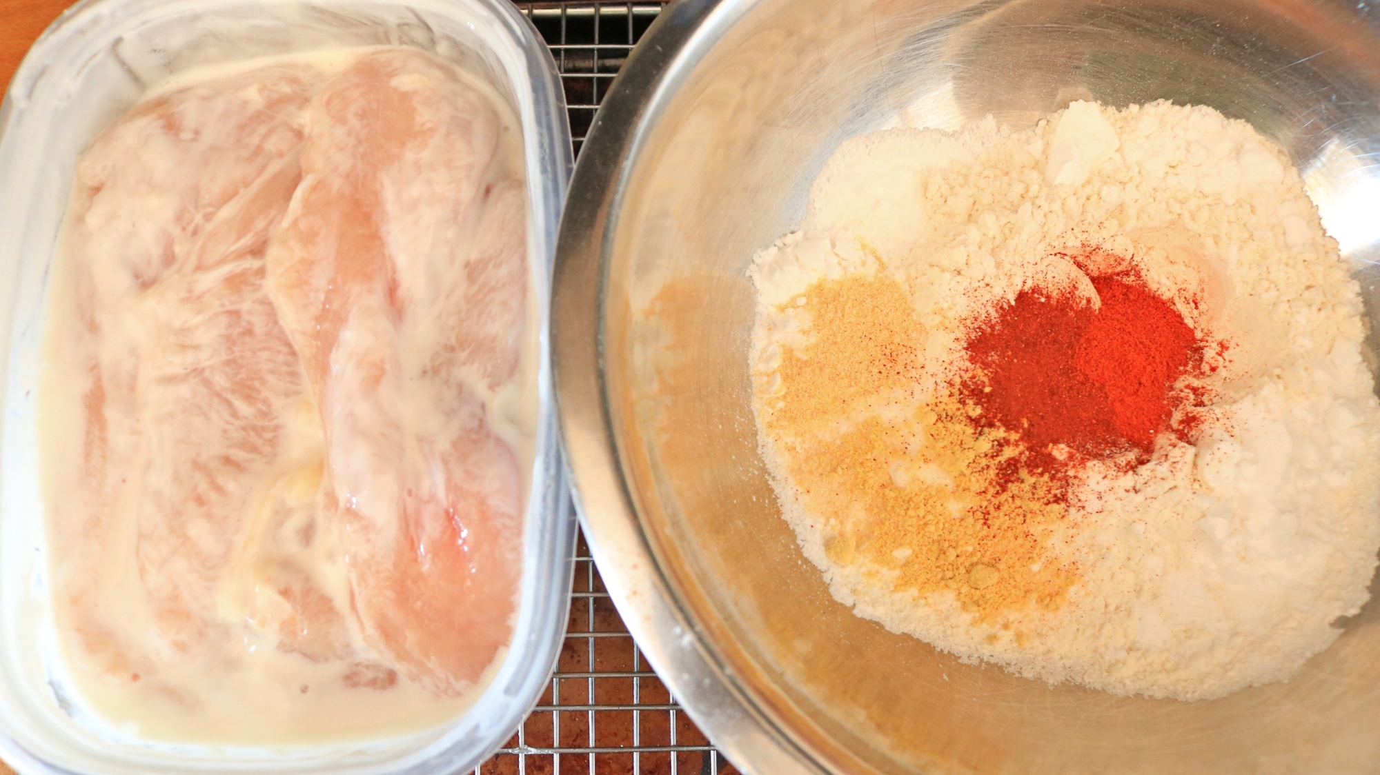 A container of buttermilk marinating chicken and a bowl of flour and spices.